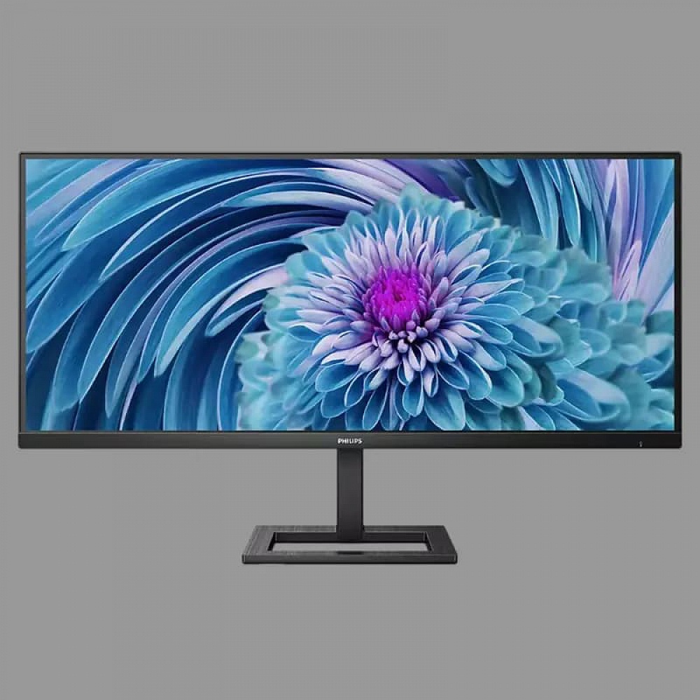 צג מחשב Philips UltraWide בעיצוב מודרני בצבע שחור, עם מסך רחב במיוחד בפורמט פנורמי ומסגרת דקה. הצג מותקן על מעמד מרכזי מלבני בעל בסיס פתוח ויציב. על המסך מוצגת תמונה צבעונית של פרח בגווני כחול, טורקיז וסגול, המדגישה את שטח התצוגה הרחב ואת המראה האלגנטי של